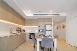 Une cuisine moderne dotée d’appareils électroménagers intégrés, un coin repas avec une table et des chaises, et un four à micro-ondes posé sur le plan de travail.