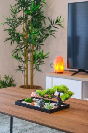 Uma árvore bonsai sobre uma mesa de madeira, com uma televisão e um aquecedor ao fundo.