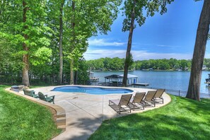Ein Garten mit Swimmingpool, Liegestühlen und einer anlegenden Mole im See.