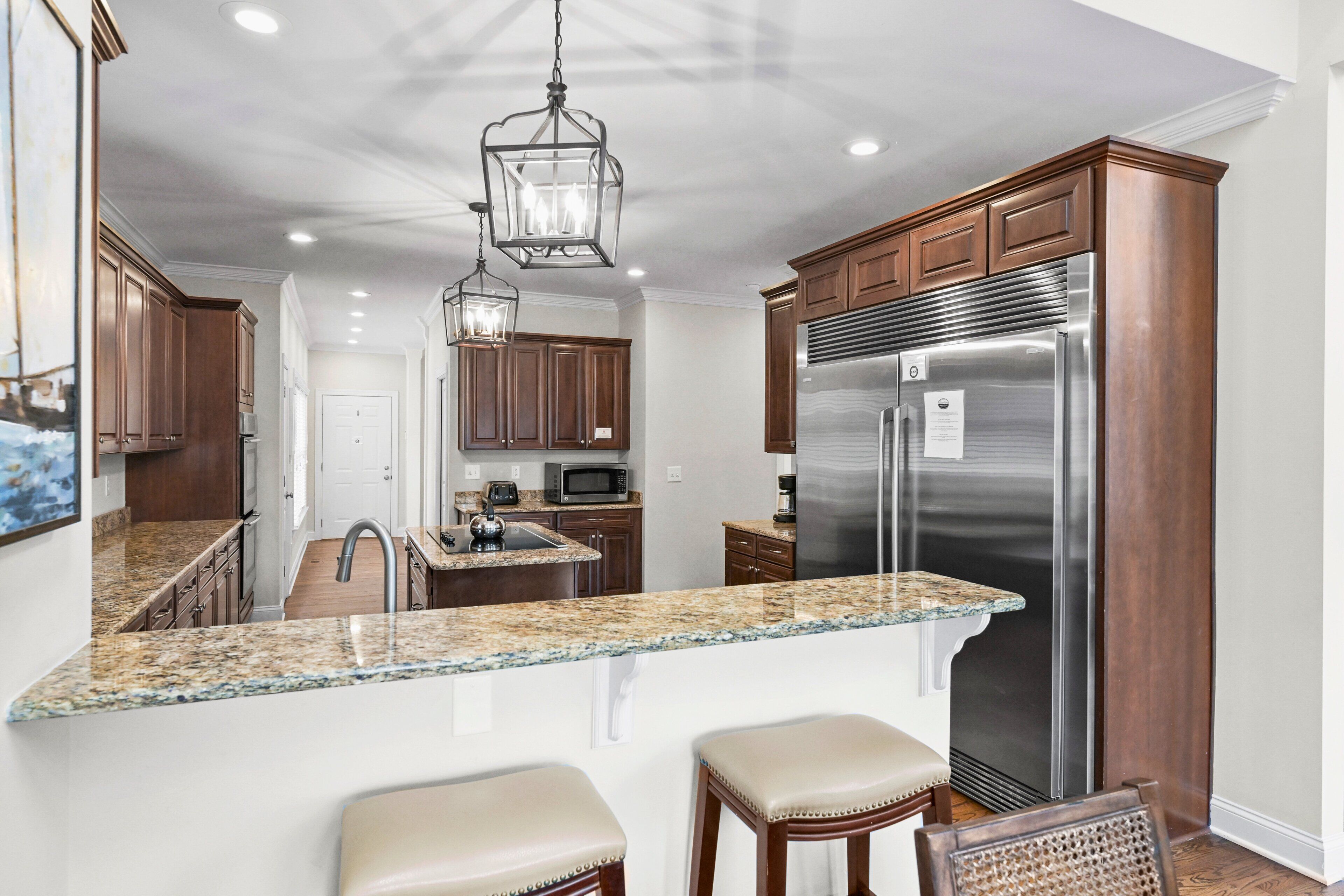 A kitchen with granite countertops, stainless steel appliances, wooden cabinets, and a hanging light fixture.