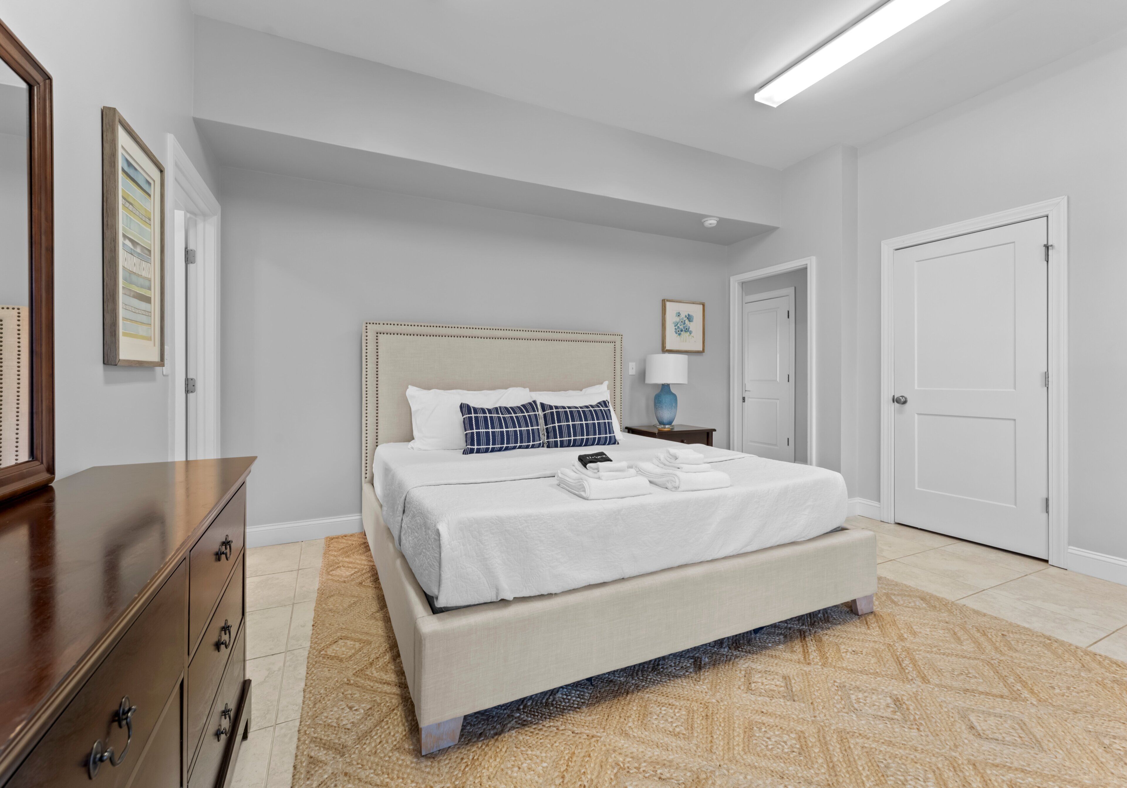 Une chambre à coucher avec un lit, une commode, une table de chevet, une lampe et une porte.