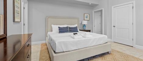 Une chambre à coucher avec un lit, une commode, une table de chevet, une lampe et une porte.