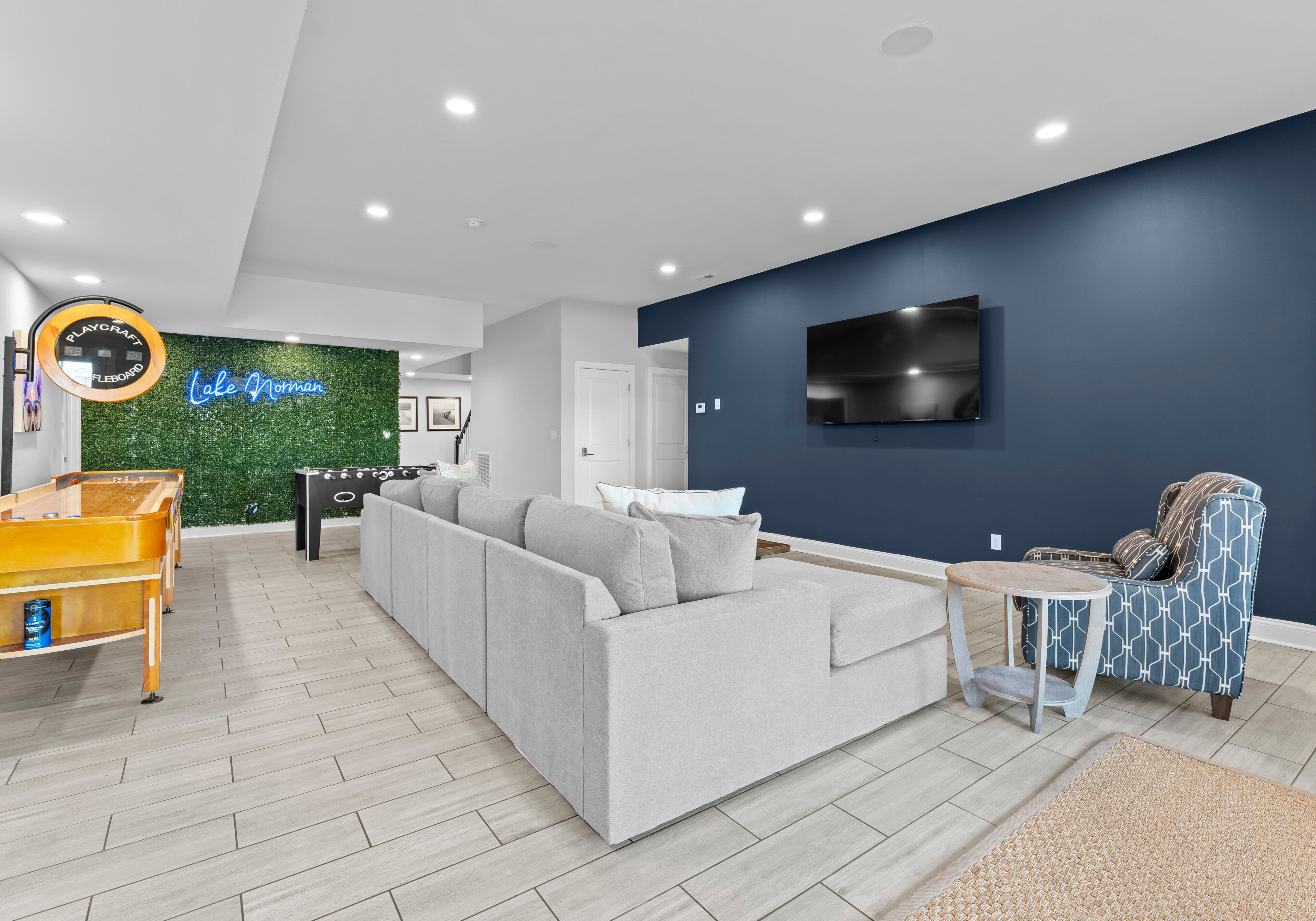 Een moderne woonkamer met een grijze bank, een kleine tafel, een blauwe fauteuil met een patroon, een pooltafel en een neonbord.