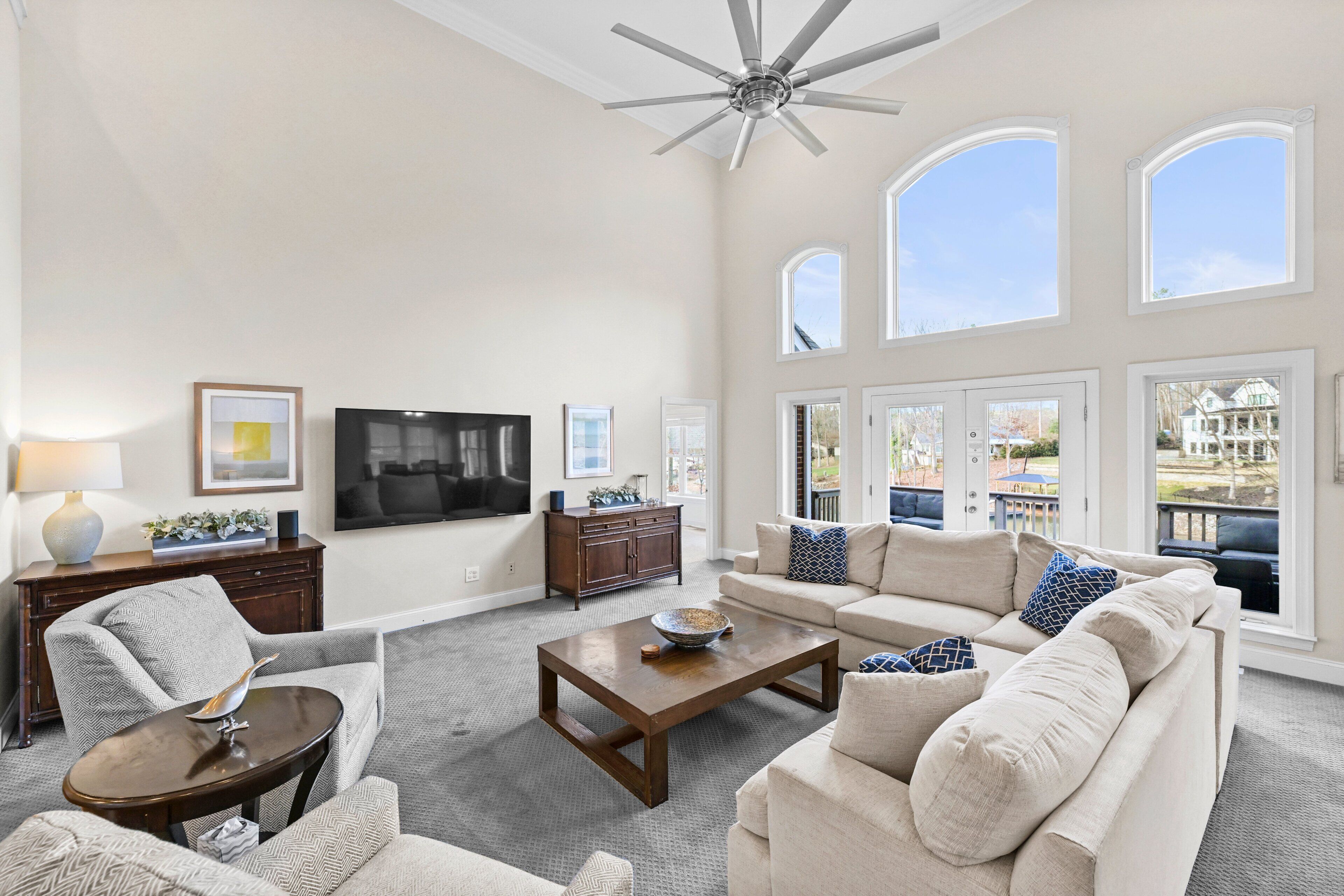 A spacious living room with a ceiling fan, large windows, a flat-screen TV, and a fireplace.