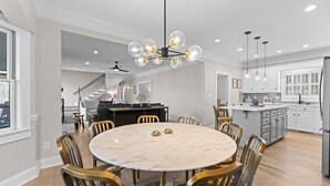 Cozinha espaçosa com armários brancos, uma ilha central e um espaço de refeições com mesa de mármore e cadeiras douradas.