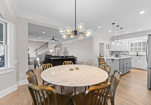 Una cocina amplia con armarios blancos, una isla central y un comedor con mesa de mármol y sillas doradas.