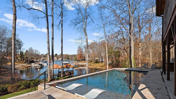 Piscina ao ar livre com espreguiçadeiras, um píer e vista para um lago e árvores.