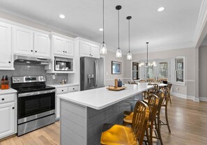 Una cocina moderna con electrodomésticos de acero inoxidable, armarios blancos y una isla central con taburetes de bar.