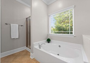 Un baño con bañera, ducha y ventana con persianas.