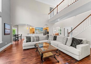 Ein geräumiges Wohnzimmer mit einem Ecksofa, einem Glastisch und einer Treppe.