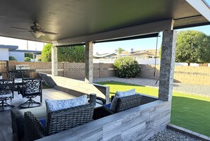 Ein überdachter Patio-Bereich mit Gartenmöbeln, einem Deckenventilator und Blick auf den Garten.