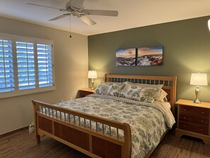 Ein Schlafzimmer mit einem hölzernen Bett, zwei Nachttischen mit Lampen, einem Deckenventilator und einem Fenster mit Jalousien.