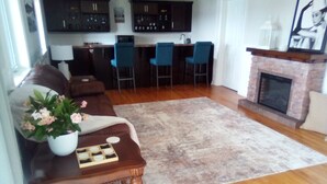 Ein Wohnzimmer mit einer Couch, einem Couchtisch mit Blumenvase, einem Kamin und einer Küche im Hintergrund.