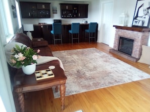 A living room with a sofa, a coffee table with a vase of flowers, a fireplace, and a kitchen in the background.