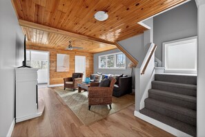 A spacious room with a wooden ceiling, a staircase, and a view of the outdoors.
