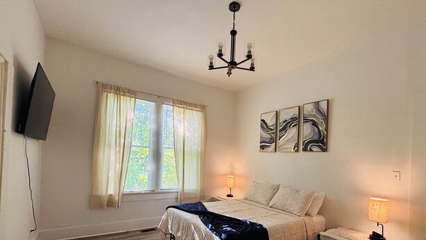 A bedroom with a bed, bedside lamps, a TV, and artwork on the wall.