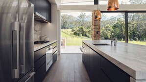 Een moderne keuken met een groot eiland, roestvrijstalen apparatuur en uitzicht op een bebost landschap.