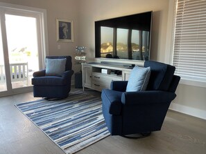 Ein Wohnzimmer mit zwei blauen Sesseln, einem großen Flachbildfernseher, einer Holzkassette und einem Streifen Teppich.