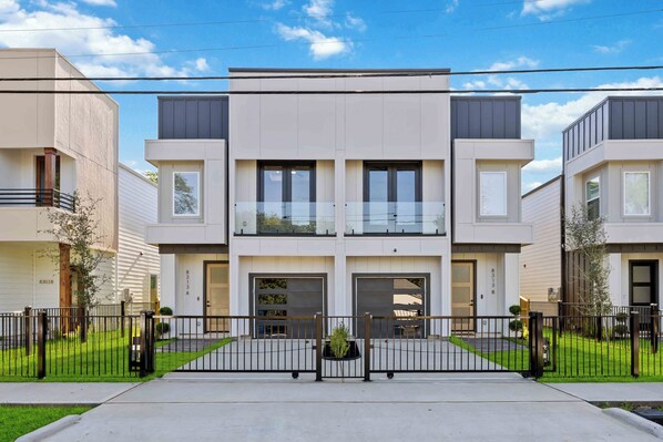 Un moderno edificio residenziale a più piani con ingresso centrale, due garage e un piccolo balcone.