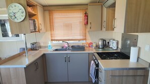 A compact kitchen with a sink, stove, and wooden cabinets. - 3-bed Caravan, Sleeps 8 With Enclosed Decking (Fleetwood)