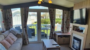 A cozy living room with a sofa, a coffee table, a TV, and a fireplace. - 3-bed Caravan, Sleeps 8 With Enclosed Decking (Fleetwood)