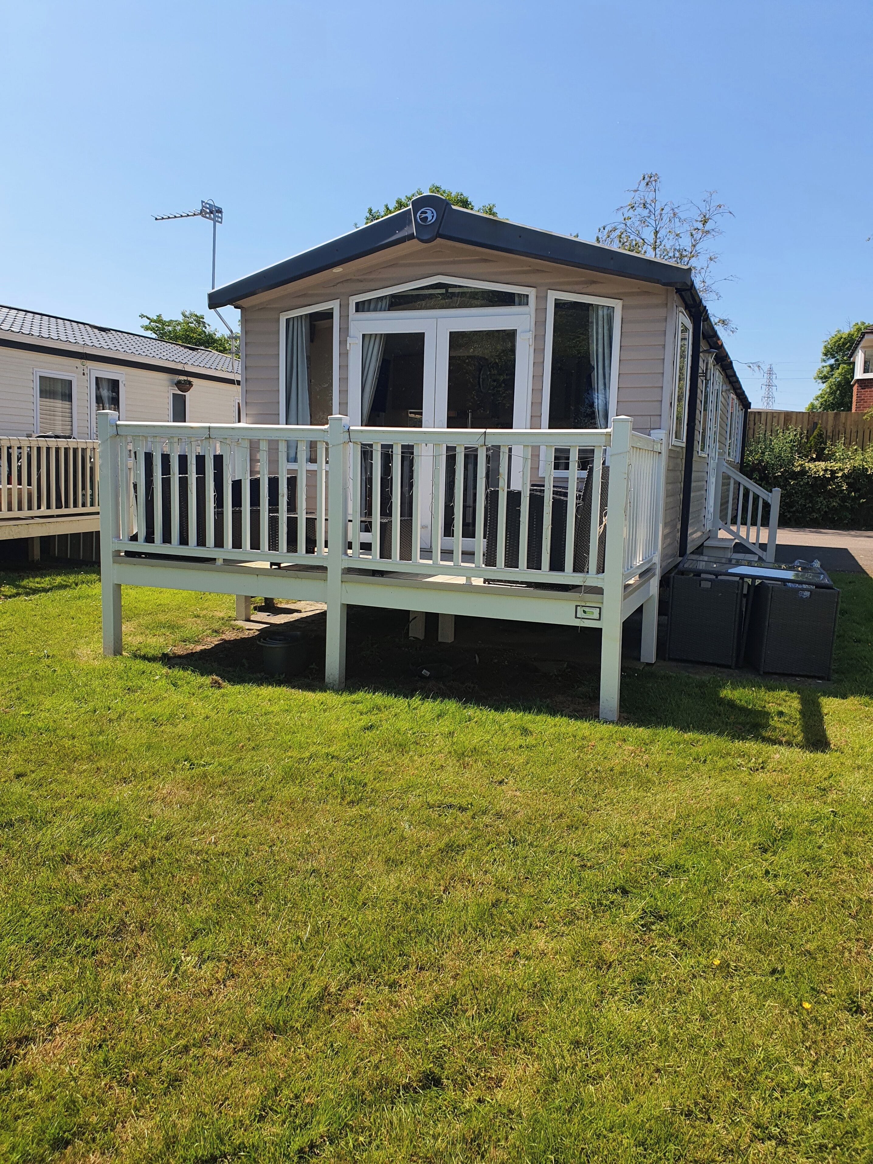 Ein Mobilheim mit eingezäunter Terrasse, überdachter Veranda und kleinem Garten.