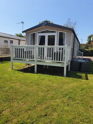 A mobile home with a fenced deck, a covered porch, and a small garden area. - 3-bed Caravan, Sleeps 8 With Enclosed Decking (Fleetwood)
