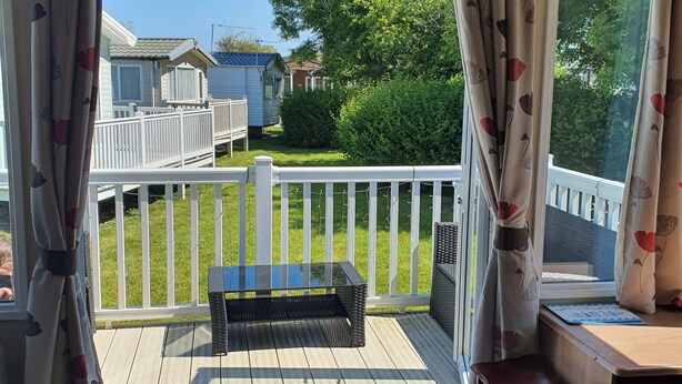 A covered outdoor deck with a table and chairs, a view of a house, and a white fence. - 3-bed Caravan, Sleeps 8 With Enclosed Decking (Fleetwood)