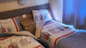 A hotel room with two beds, a wooden headboard, a shelf with a sign, and a window with curtains. - 3-bed Caravan, Sleeps 8 With Enclosed Decking (Fleetwood)