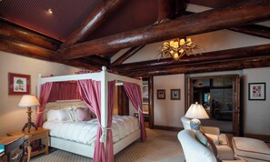 Una cama con dosel y cortinas rojas, un candelabro y un techo de madera.