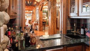 A rustic kitchen with wooden cabinets, a marble countertop, and a view into the dining area. - Private Sun Valley Lodge | Walk to Lift + Hot Tub (Ketchum)