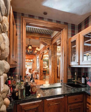 A rustic kitchen with wooden cabinets, a marble countertop, and a view into the dining area.