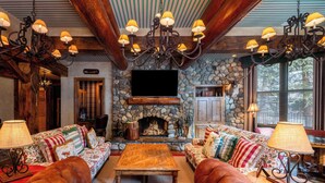 A cozy living room with a stone fireplace, leather sofas, and a chandelier. - Private Sun Valley Lodge | Walk to Lift + Hot Tub (Ketchum)
