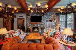 A cozy living room with a stone fireplace, leather sofas, and a chandelier.