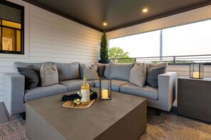 Ein moderner Außenbereich mit einer grauen Couch, einem Holztisch mit Flasche und Gläsern sowie einer Kerze.