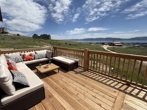 Une terrasse avec un canapé et des coussins, une petite table et une vue sur un paysage comprenant des maisons et des montagnes.