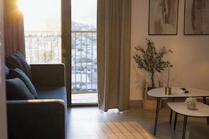 Ein Wohnzimmer mit einer Couch, einem kleinen Tisch, einer Topfpflanze und Blick durch ein Fenster.