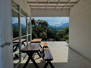 An outdoor patio with wooden tables and benches, large windows offering a view of a mountainous landscape.