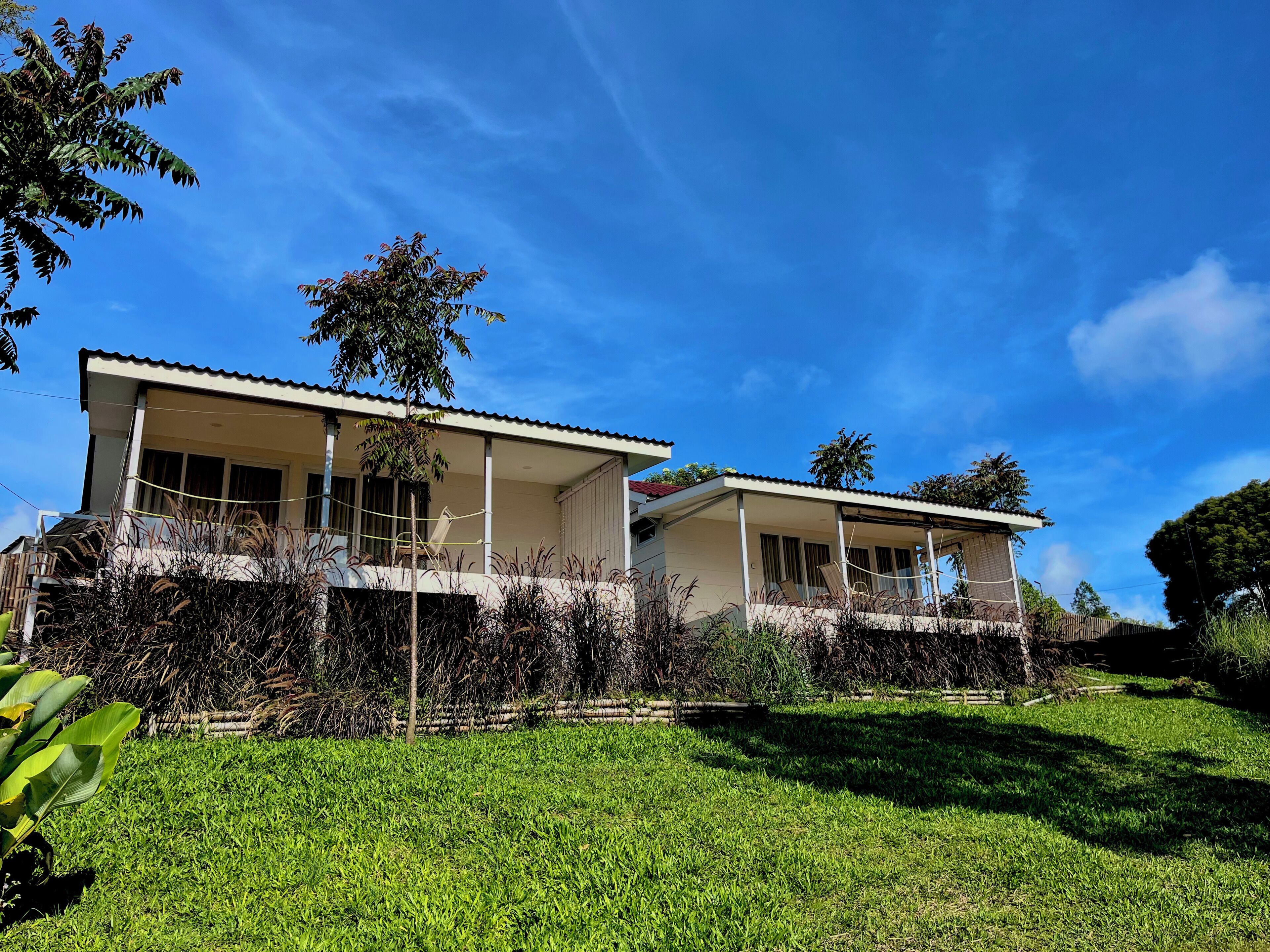 A two-story house with a balcony, surrounded by greenery and a clear blue sky.