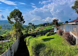 A rural landscape with a wooden fence, a small white building with a red roof, and lush greenery.