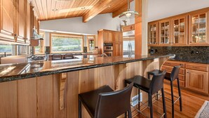 Eine moderne Küche mit Holzausziehtüren, einer Granit-Arbeitsplatte und Barhocker.