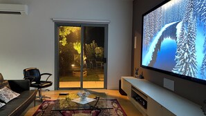 A modern living room with a large flat-screen TV, a glass coffee table, a sofa, and a sliding glass door leading to an outdoor area. - Luxury Paradise Country Suite, Nature Retreat and Private Chef Fine dining (Duffys Forest)