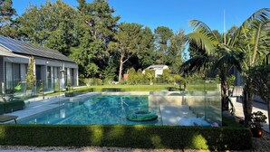 A swimming pool with a glass enclosure, surrounded by a well-maintained hedge, palm trees, and a clear blue sky. - Luxury Paradise Country Suite, Nature Retreat and Private Chef Fine dining (Duffys Forest)