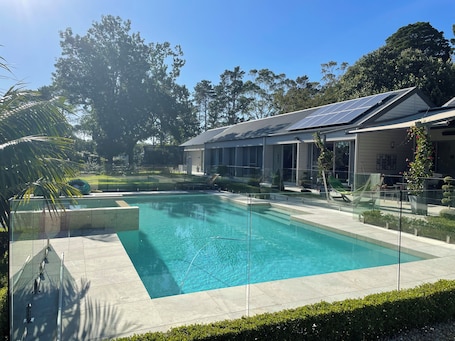 A swimming pool with a glass enclosure, a modern house with solar panels, and a well-maintained lawn.. Luxury Paradise Country Suite, Nature Retreat and Private Chef Fine dining