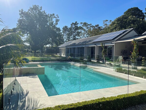 Una piscina con cerramiento de vidrio, una casa moderna con paneles solares y un césped bien cuidado.
