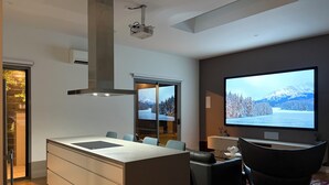 A modern kitchen with a central island, a large flat-screen TV, and a dining area with a sofa and chairs. - Luxury Paradise Country Suite, Nature Retreat and Private Chef Fine dining (Duffys Forest)