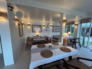 Un coin repas avec une table dressée pour quatre personnes, entourée de chaises, agrémenté de lampes fixées au mur et de tableaux encadrés.
