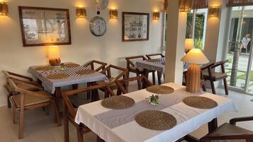 A dining area with wooden tables and chairs, framed nautical artwork on the walls, and a view of the outdoors through large windows.