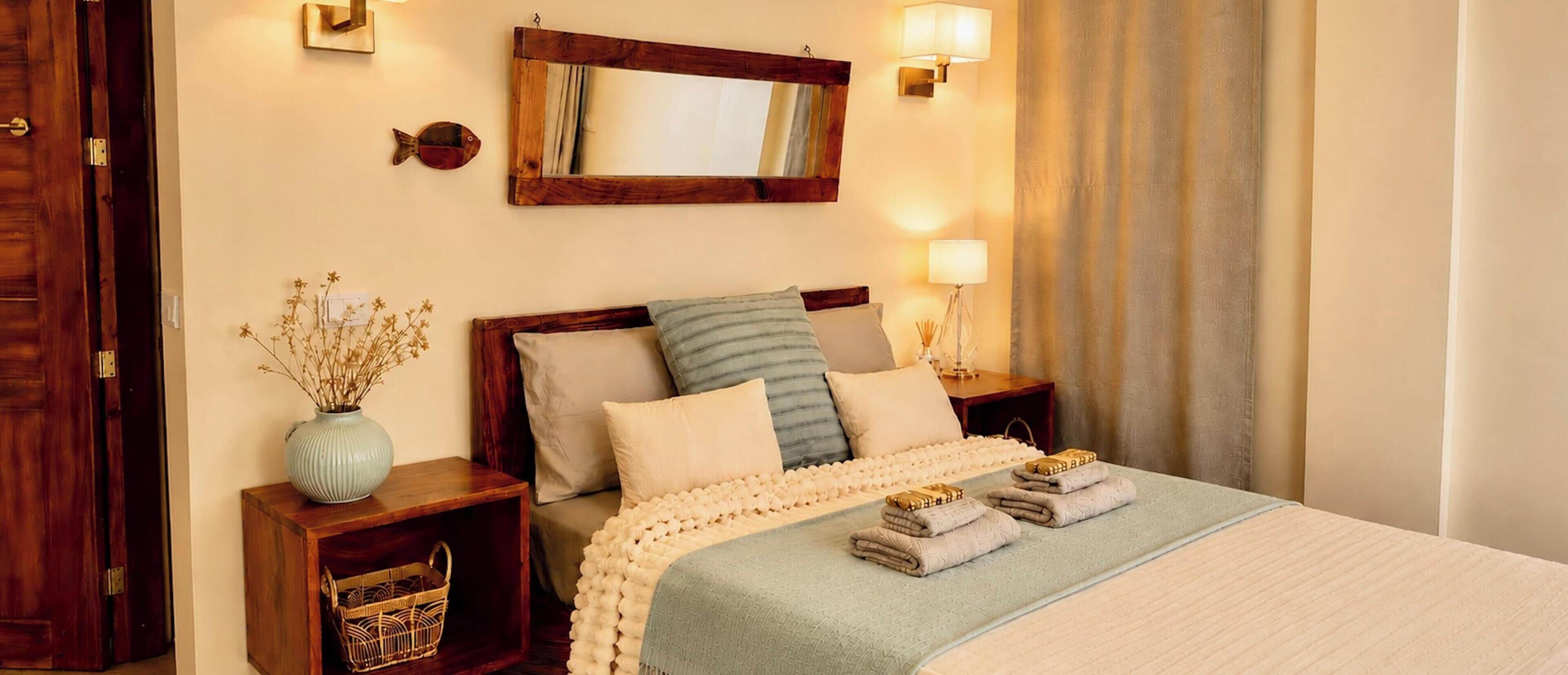 Habitación de hotel ordenada con cama, mesitas de noche, un espejo y una ventana con cortinas.