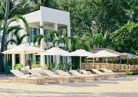 A beachside resort with lounge chairs, umbrellas, and a modern building.. Binucot Pearl Boutique Resort